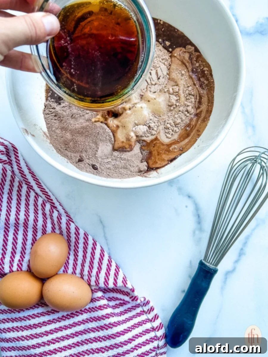 Dr. Pepper soda being poured into a white mixing bowl containing the dry ingredients for the cake, illustrating the start of the mixing process.
