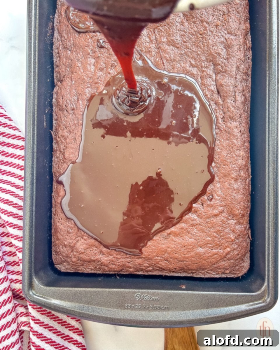 Thick, glossy chocolate fudge frosting being poured generously over the warm Dr. Pepper cake, still in its pan, ready to set and soak in.