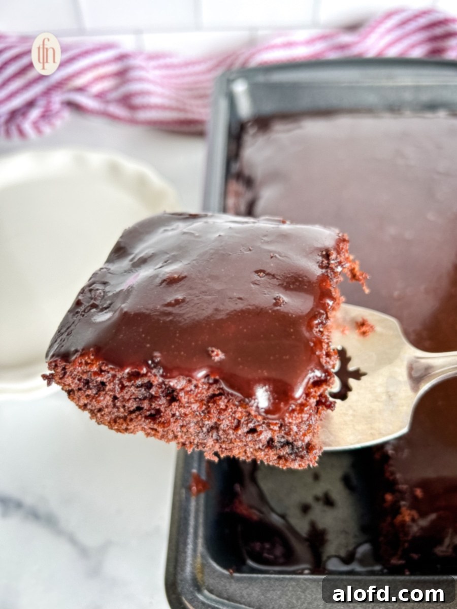 A silver serving spoon holds a generous slice of the frosted Dr. Pepper chocolate cake directly over the baking pan, ready to be placed on a plate.