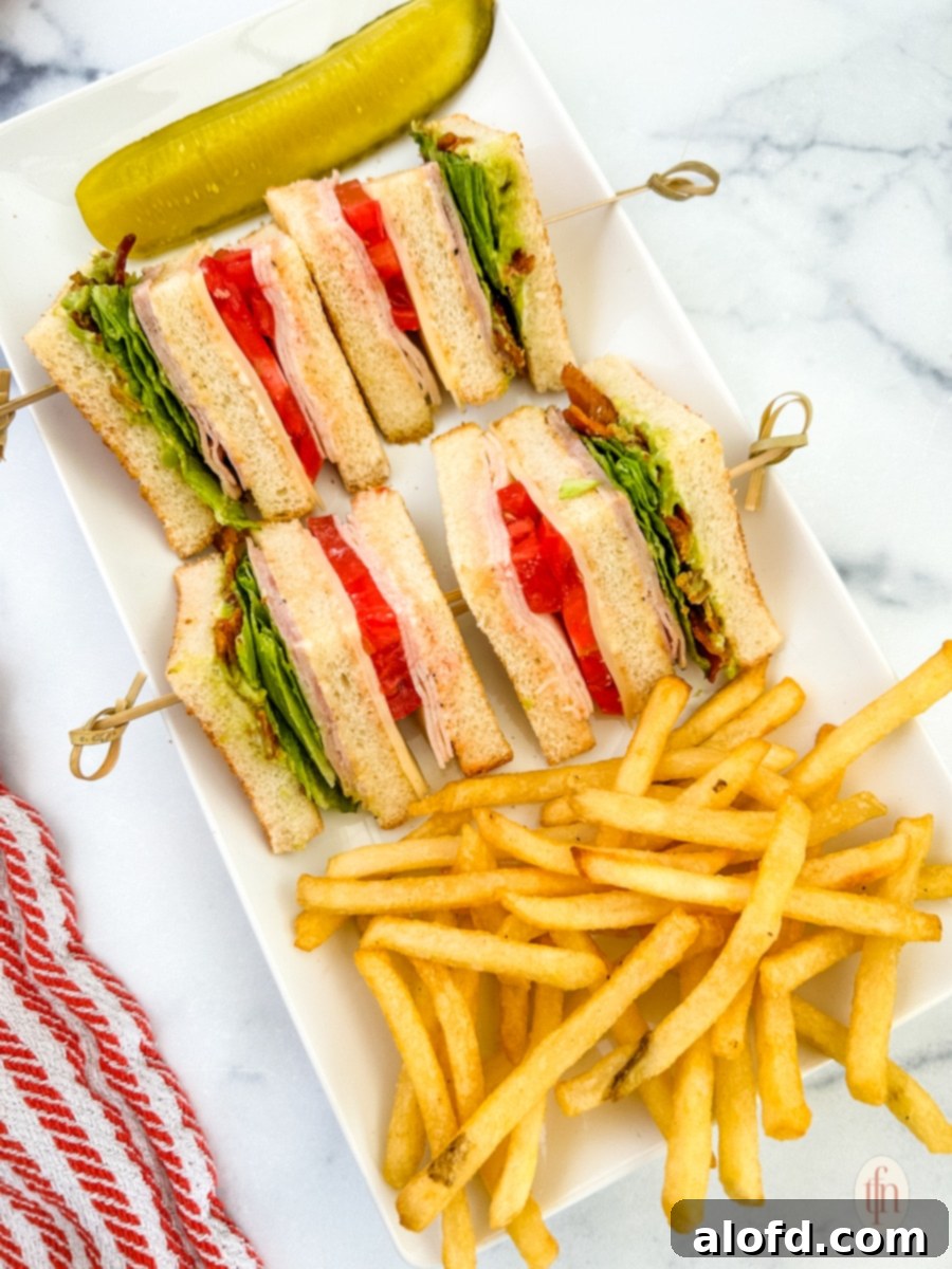 Four slices of a chicken club sandwich with sticks and fries on a white plate.