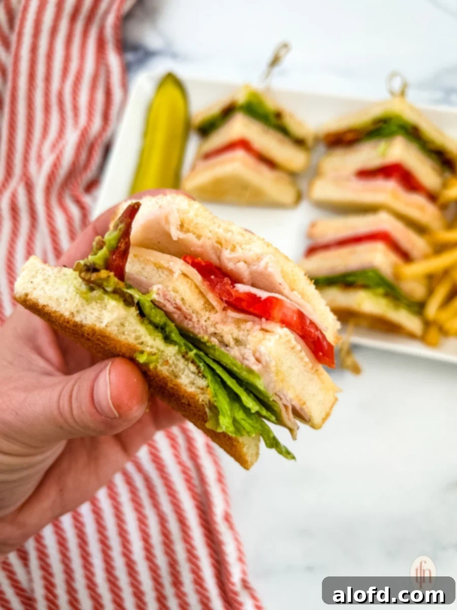 Chicken club sandwich handled by one hand.