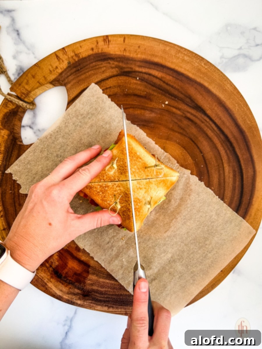 Slicing the chicken club sandwich on a round wooden board with parchment paper.