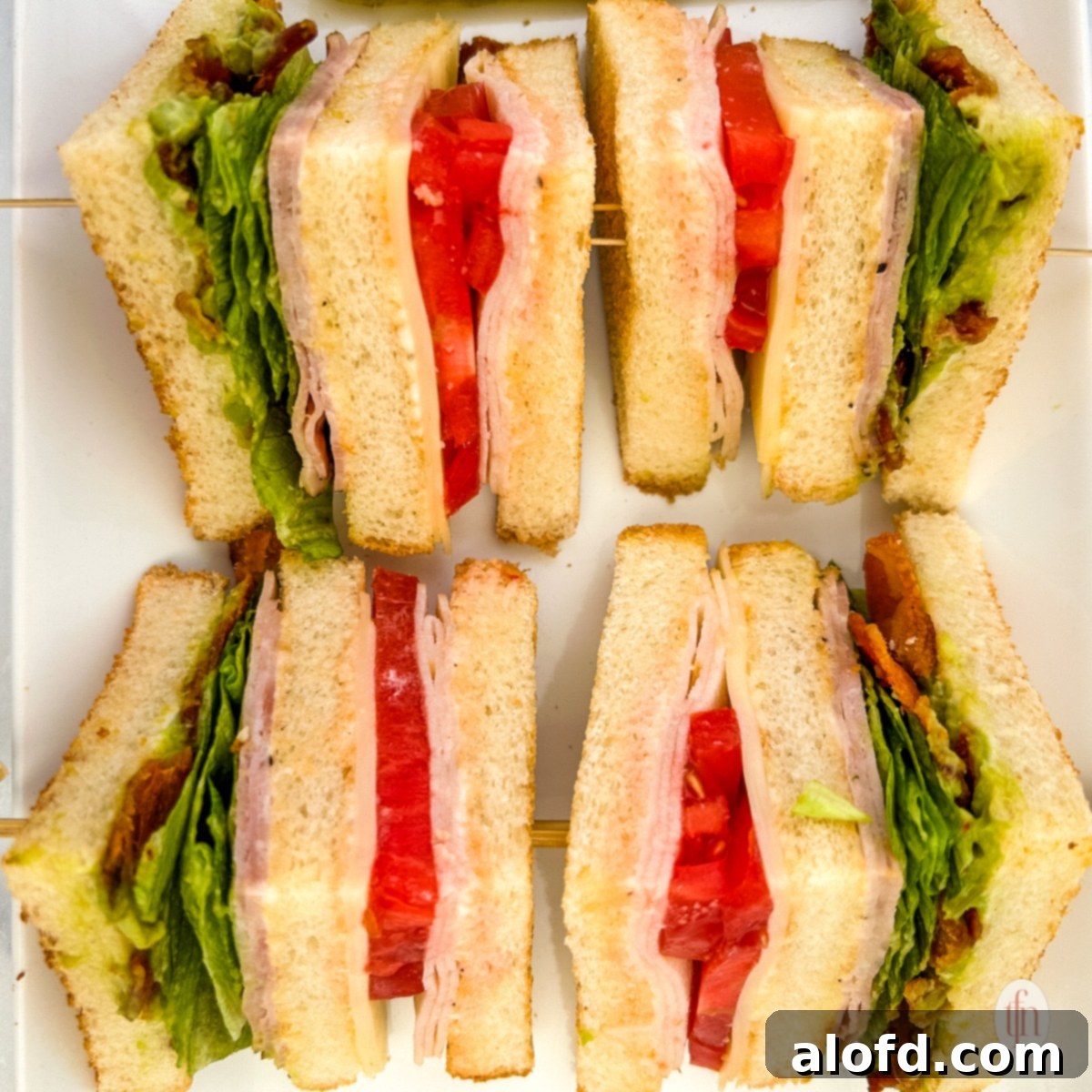 Four slices of chicken club sandwich on a white plate.