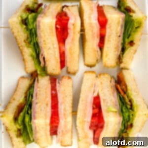 Four slices of chicken club sandwich on a white plate.