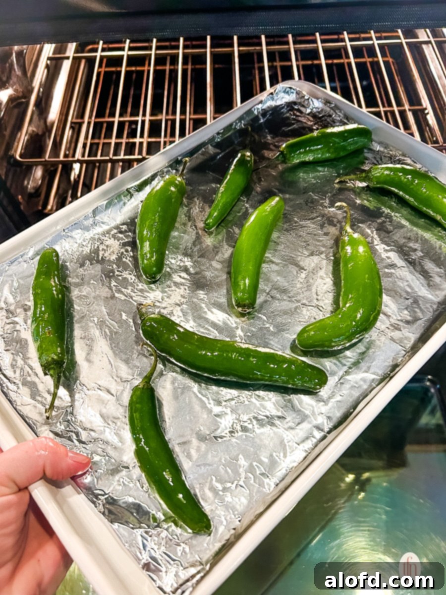 Woman's hand placing a sheet pan of jalapenos on oven rack, preparing to roast them.