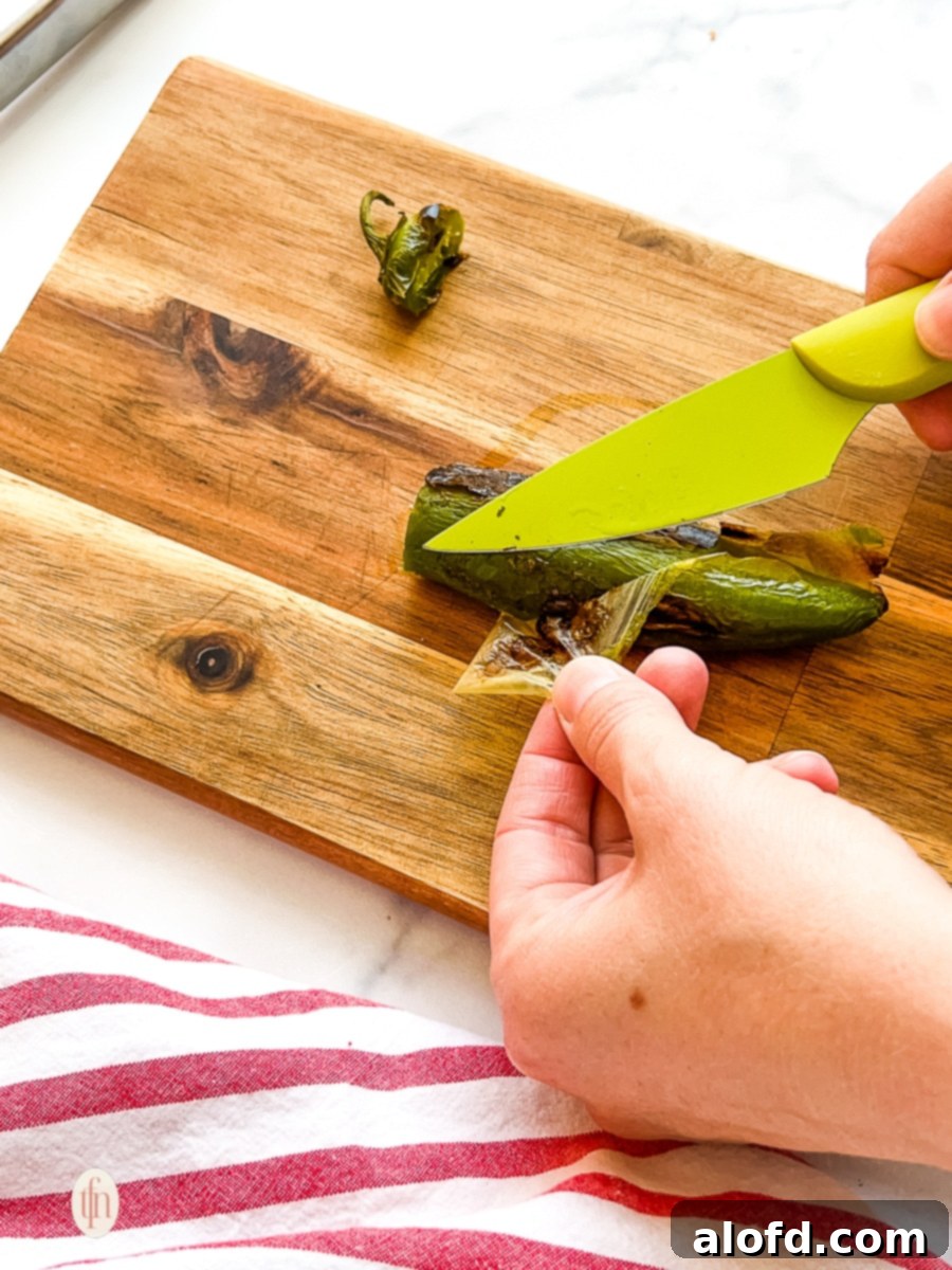 Woman using a knife to remove blistered skin from an oven roasted green pepper.