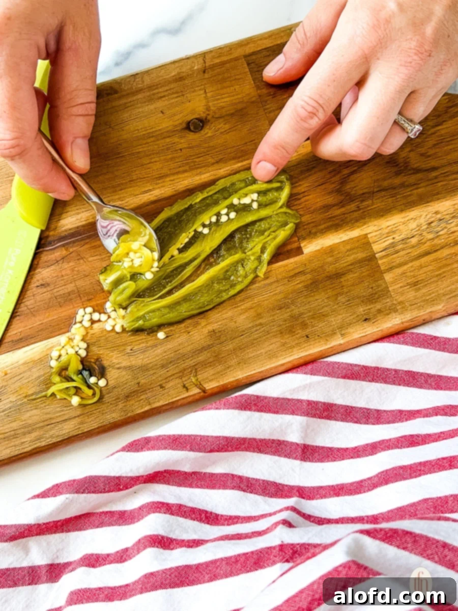Using a spoon to remove seeds from a roasted jalapeno.