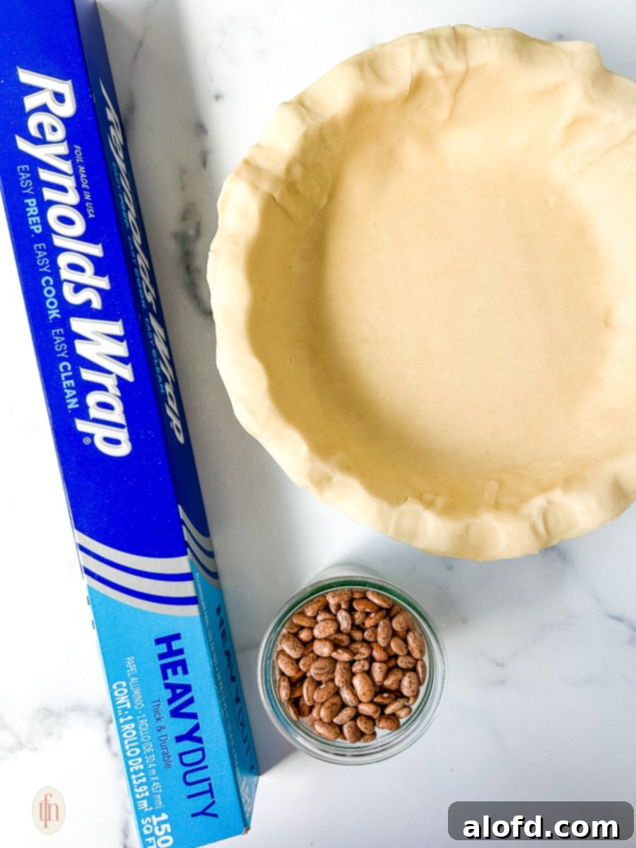 Velvety Pumpkin Custard Pie 5 Reynolds wrap next to unbaked pie crust and a jar of dried beans.