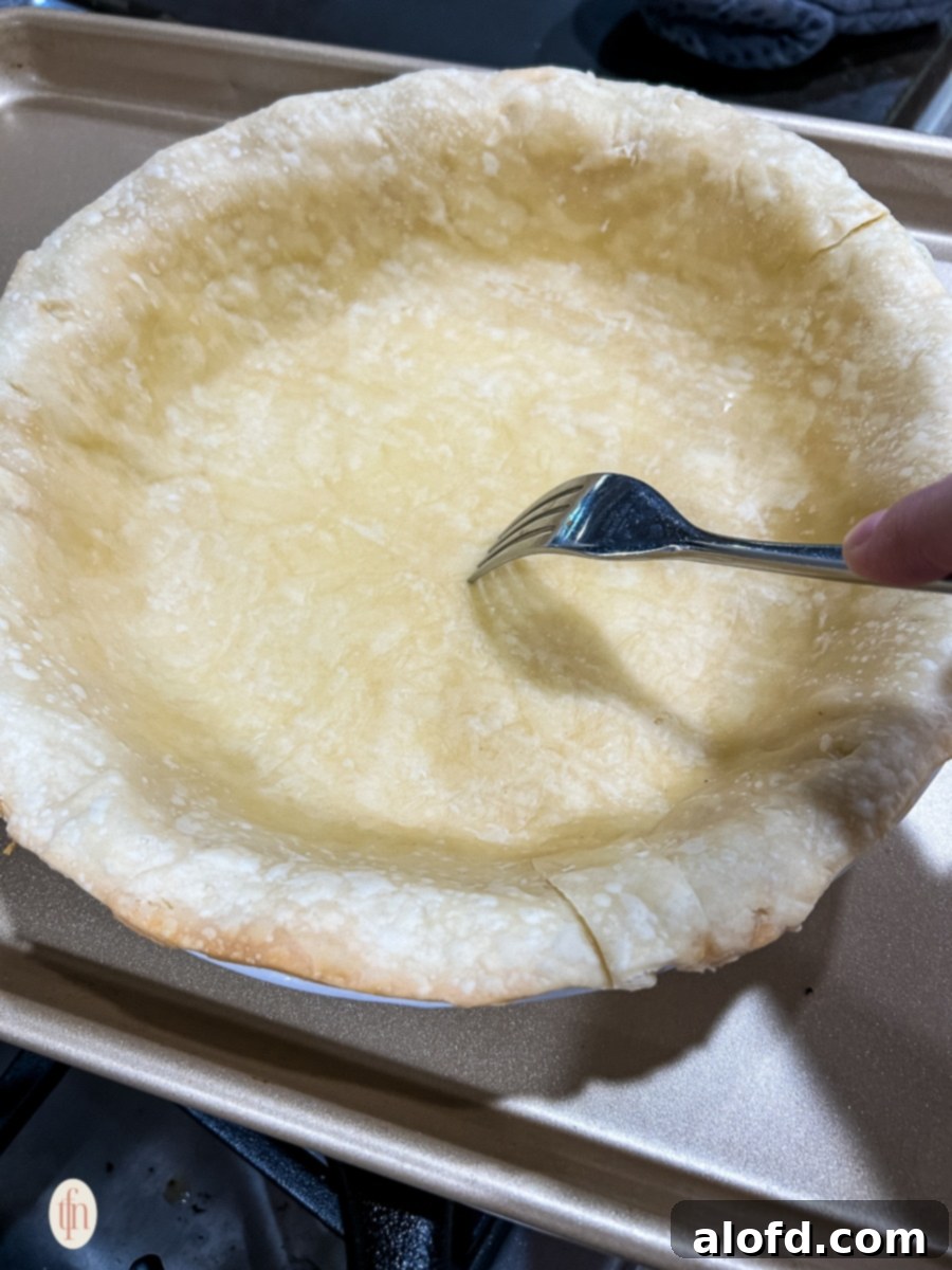 Velvety Pumpkin Custard Pie 6 Fork poking holes in a partially baked pie crust.