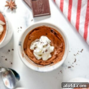 Simple Decadent Chocolate Mousse 15 One small cup of chocolate mousse topped with whipped cream on a white background.