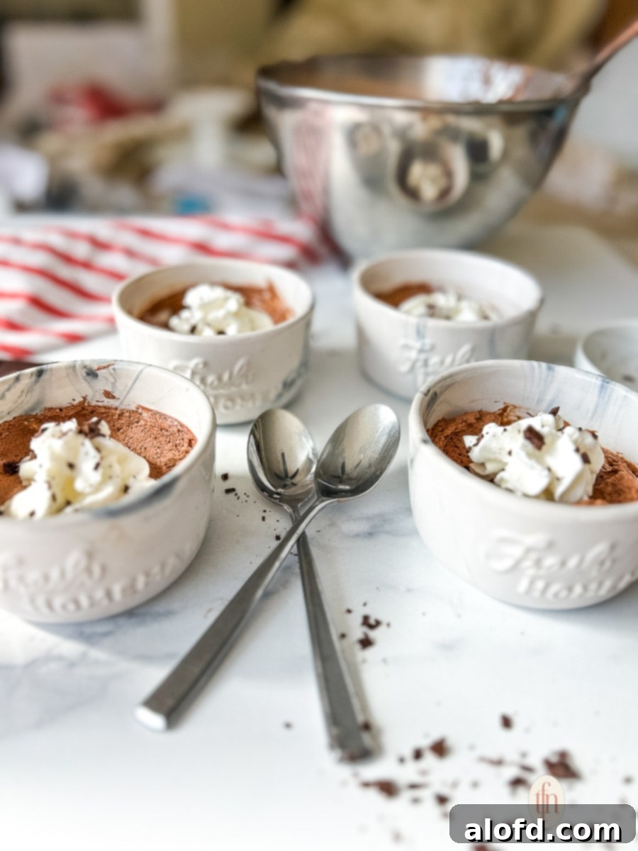Simple Decadent Chocolate Mousse 3 Individual cups filled with chocolate mousse and topped with whipped cream and shaved chocolate on a white background.