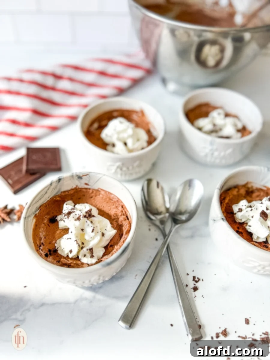 Simple Decadent Chocolate Mousse 4 Individual cups filled with chocolate mousse and topped with whipped cream and shaved chocolate on a white background.