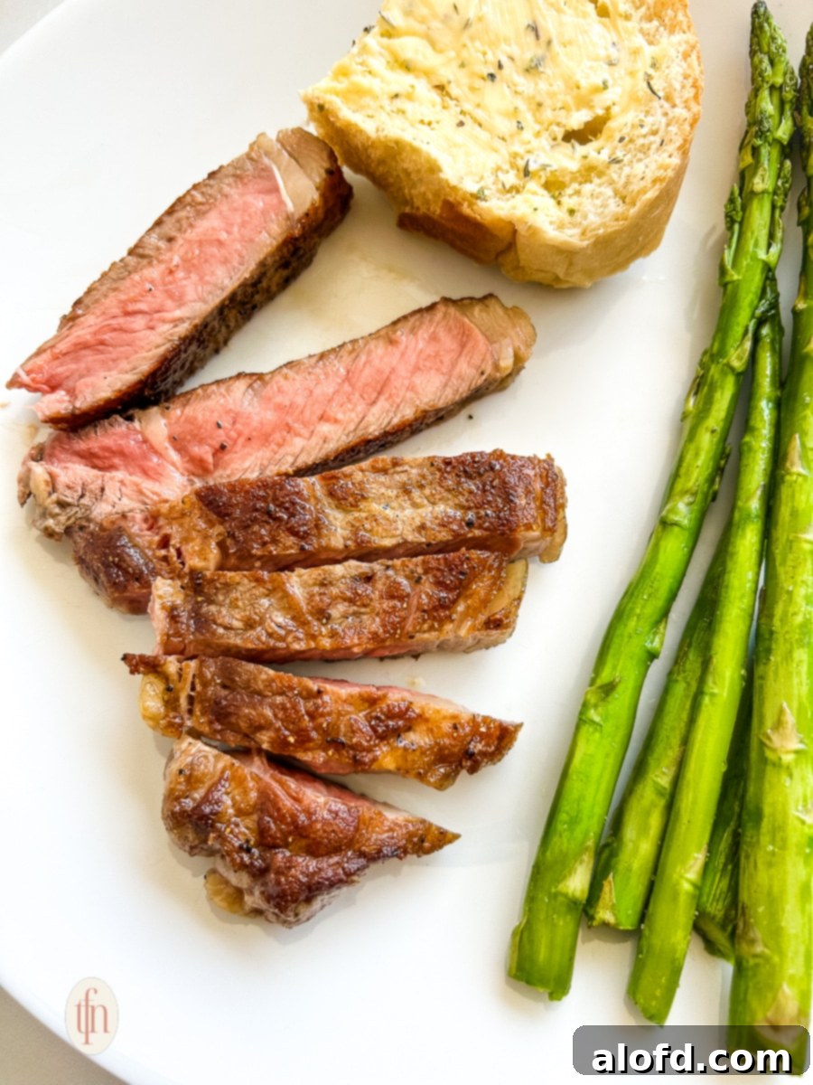Slices of grilled NY strip steak arranged on a dinner plate, accompanied by vibrant green asparagus spears and a slice of buttered bread.