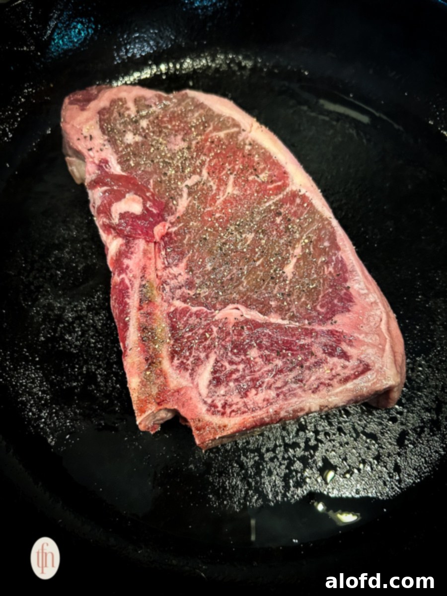 A seasoned shell steak being placed into a visibly hot, preheated cast iron skillet on a grill, creating an instant sizzle for searing.