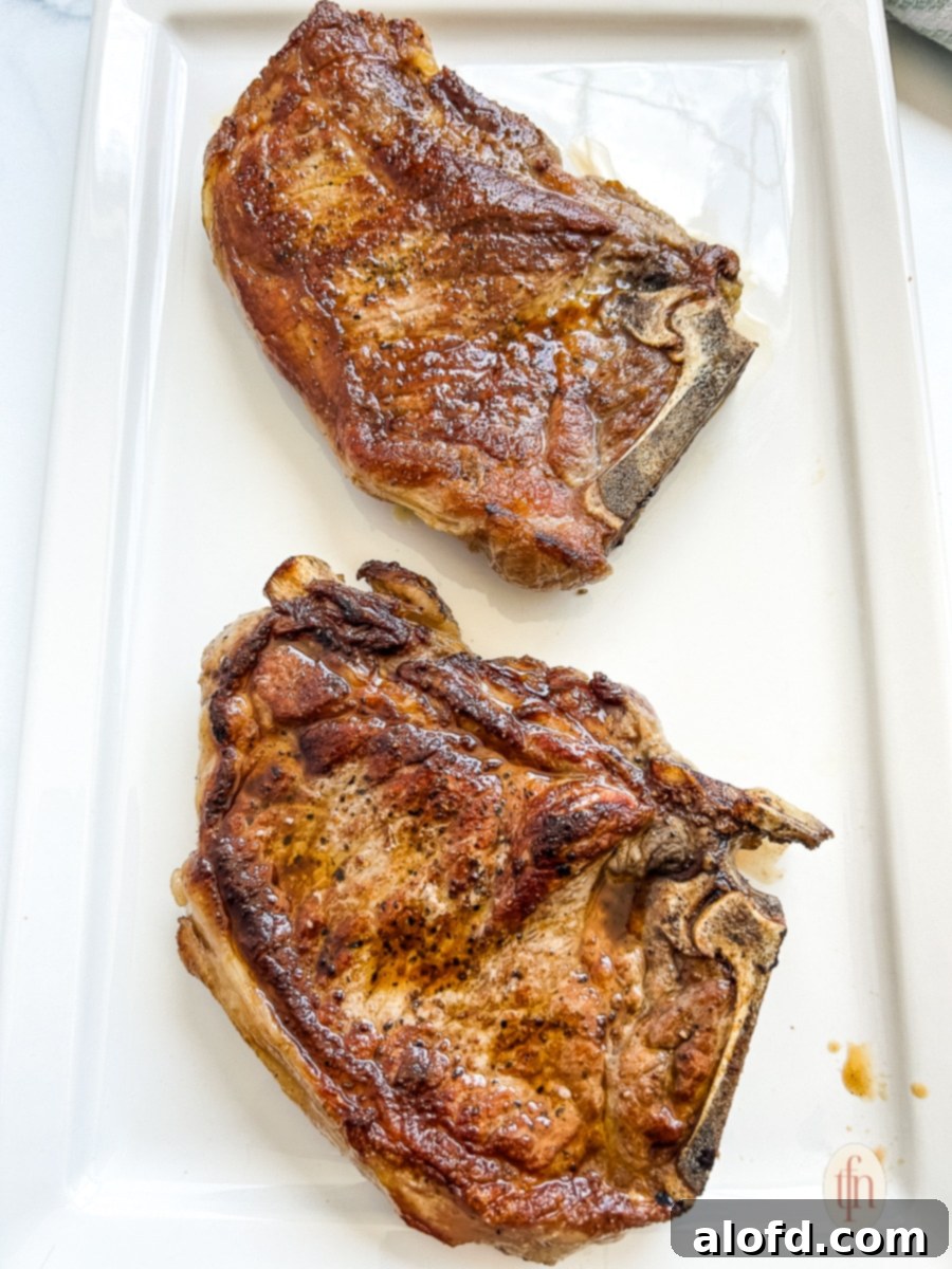 Two juicy, perfectly grilled bone-in beef steaks resting on a cutting board, lightly tented with aluminum foil to ensure optimal juiciness.