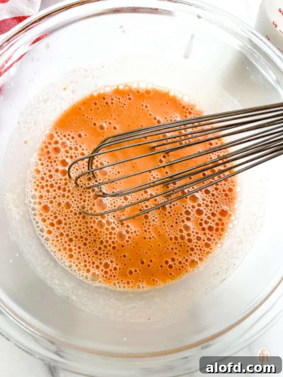 The Ultimate 3-Ingredient Tomato Soup 7 A glass bowl where heavy cream is being whisked into a small portion of tomato soup, tempering the cream.