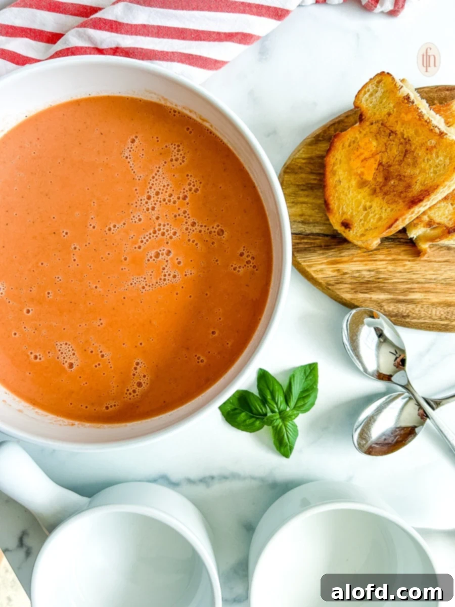 The Ultimate 3-Ingredient Tomato Soup 8 A white bowl filled with creamy 3-ingredient tomato soup, garnished with a fresh basil sprig on the side.
