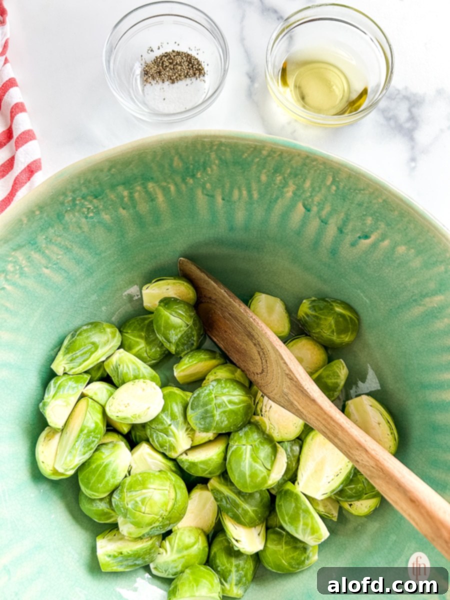 Sliced sprouts in a bowl stirred by a wooden spoon, coated with oil and seasonings.