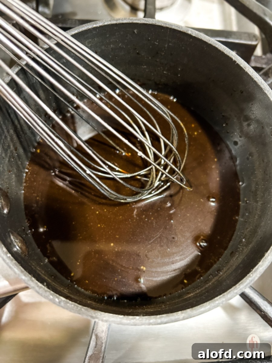 Whisking the glaze in a medium pot on the stove, showing its reduction.