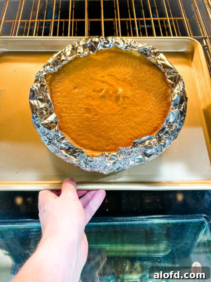 Unbaked savory pie in oven. Aluminum foil wrapped around crust. 