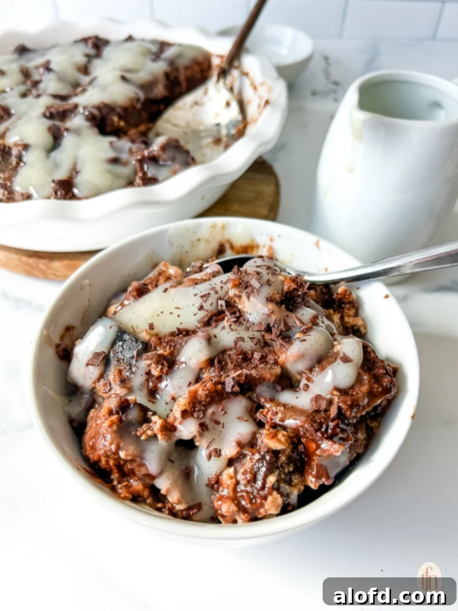 Chocolate bread pudding in a white bowl with vanilla cream sauce drizzled over the top. A truly decadent sourdough bread pudding.
