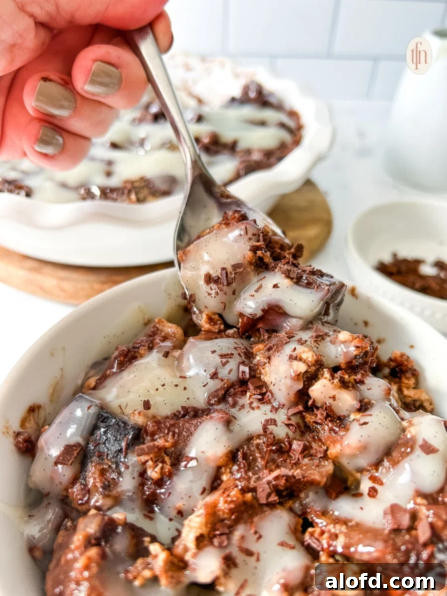 Fork lifting chocolate sourdough bread pudding from a bowl into the air, showcasing its gooey texture.