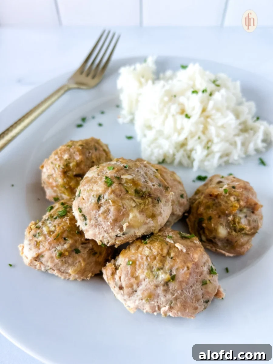 Juicy turkey zucchini meatballs on a white plate, ready to be served with a fork.