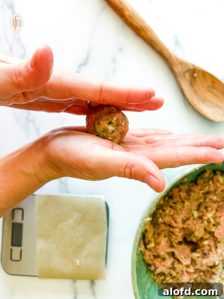 Rolling healthy zucchini meatballs in two hands over a white counter to form perfect shapes.