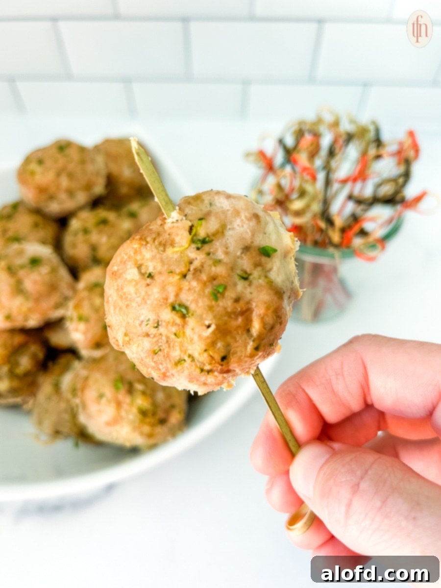 A hand holding up a healthy turkey zucchini meatball on a toothpick, highlighting its appealing texture.