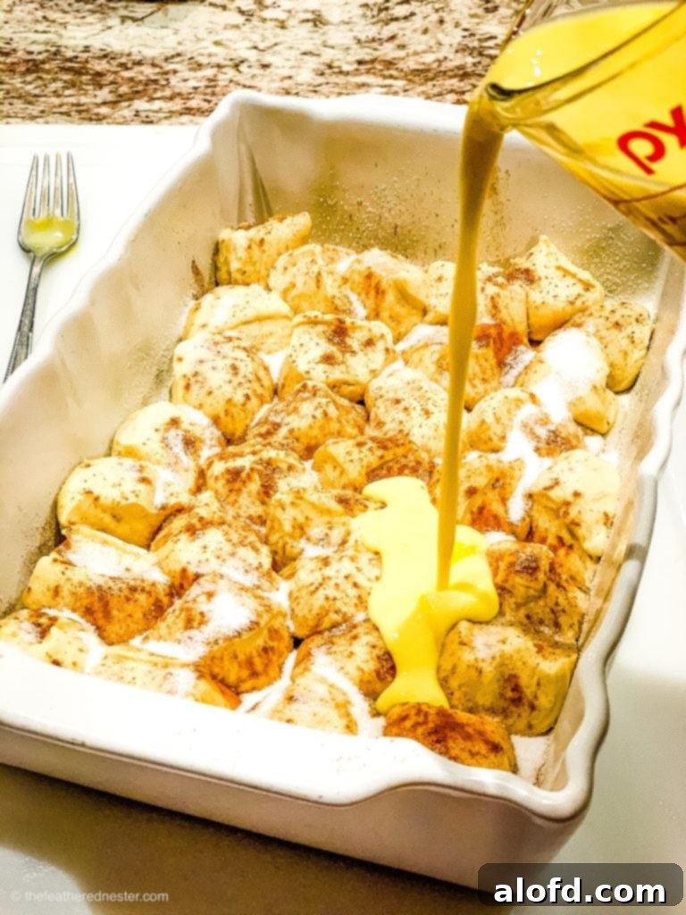 Effortless Overnight French Toast Bake 7 Hands pouring a creamy egg and milk mixture infused with maple extract and cinnamon over diced frozen dough pieces in a casserole dish.