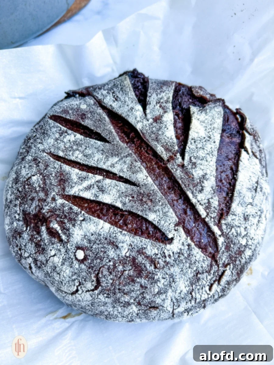Decadent Chocolate Sourdough 11 A freshly baked, rustic loaf of chocolate sourdough bread with a dark, rich crust, resting on a white surface, invitingly ready for slicing.