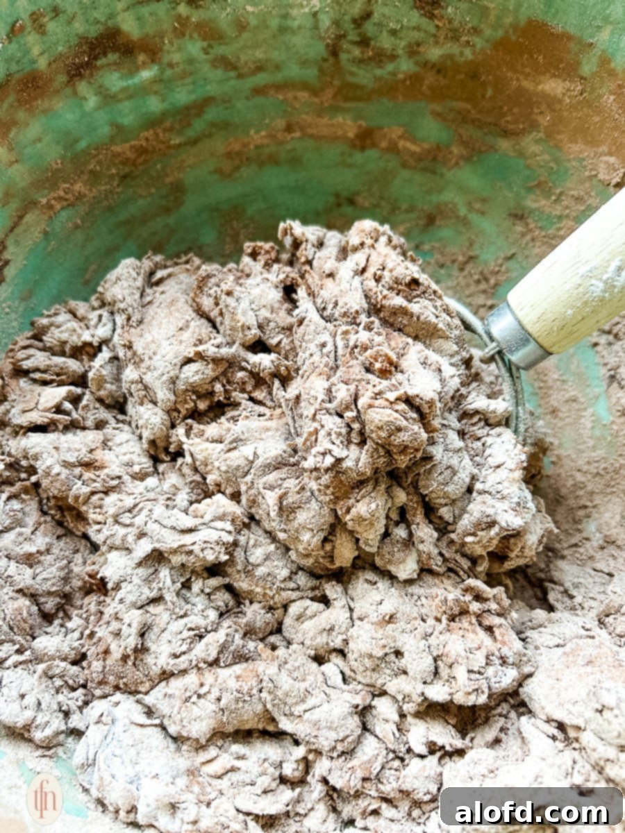 Decadent Chocolate Sourdough 5 A close-up image showing a baker gently mixing chocolate sourdough dough in a large mixing bowl with their hands, demonstrating the initial stage of dough formation.