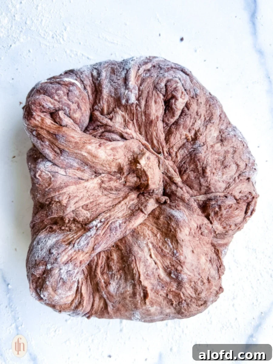 Decadent Chocolate Sourdough 6 Chocolate sourdough dough being stretched and folded on a lightly floured white surface, illustrating the gluten development technique.