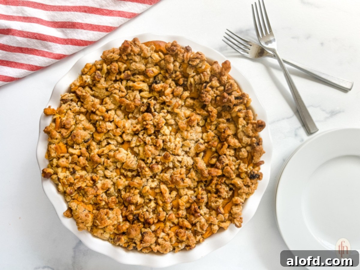 Golden Carrot Bake 3 A whole sweet carrot casserole pie with a golden oat crumble topping, next to an empty plate and two crossed forks, showcasing its tempting texture.