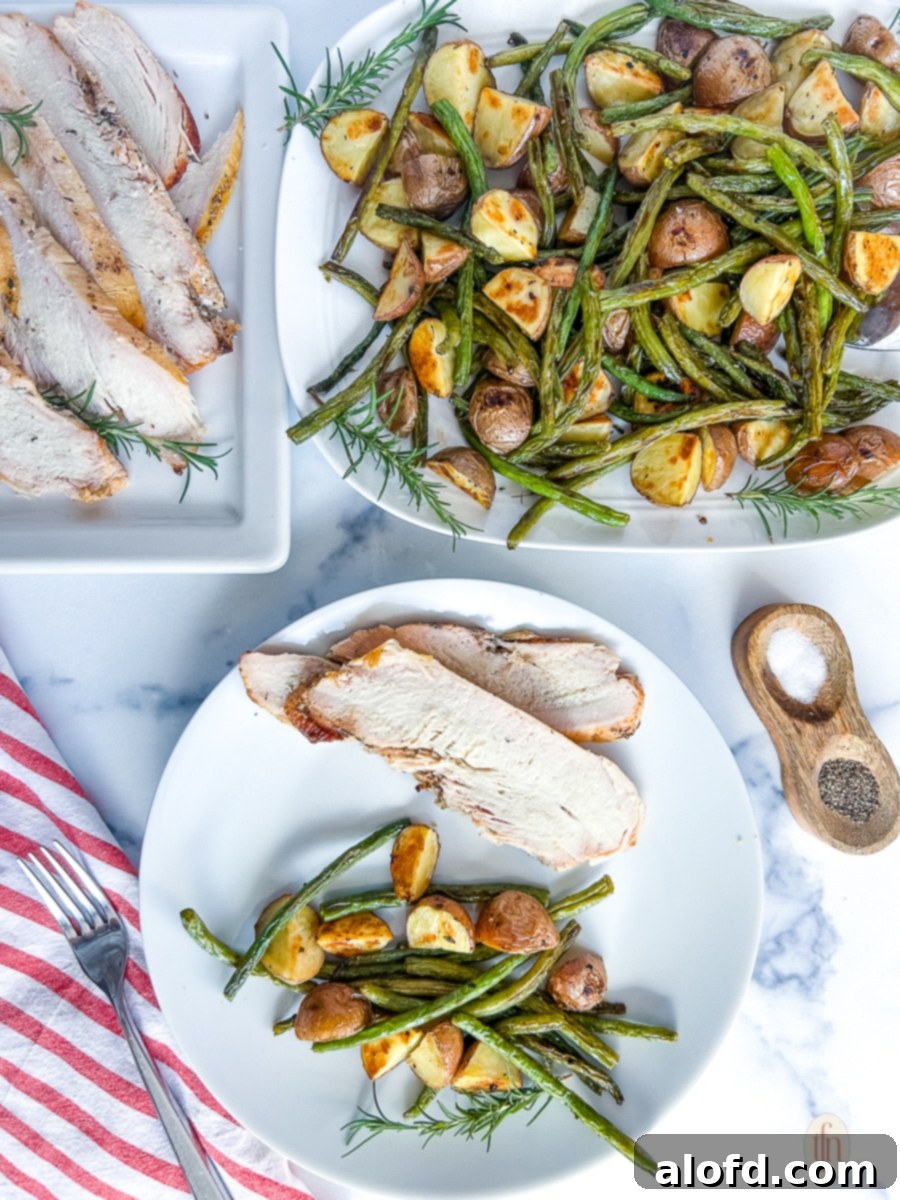 Garlic Herb Roasted Green Beans and Potatoes 3 A beautifully plated dish of roasted green beans and potatoes alongside a main course, against a clean white background.