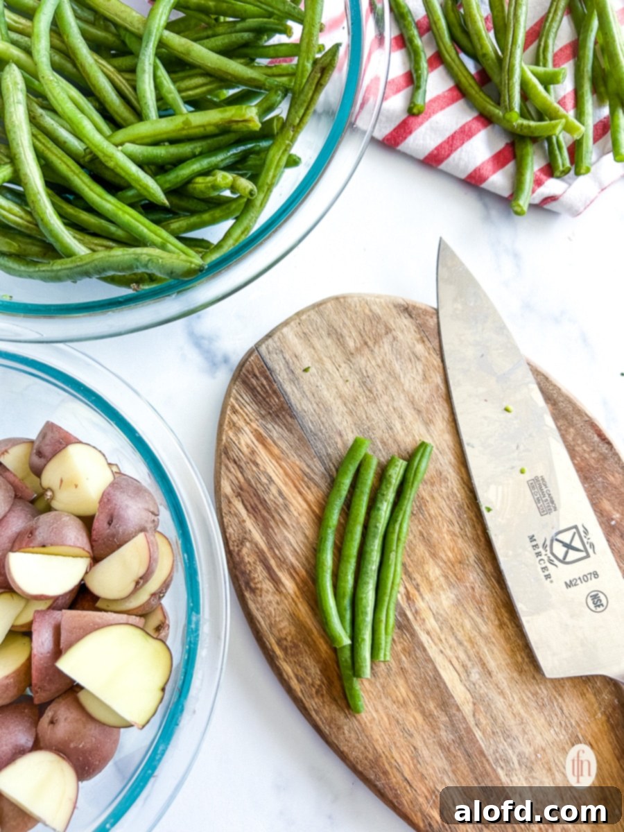 Garlic Herb Roasted Green Beans and Potatoes 5 A chef's hand cutting fresh vegetables uniformly on a cutting board, preparing them for roasting.