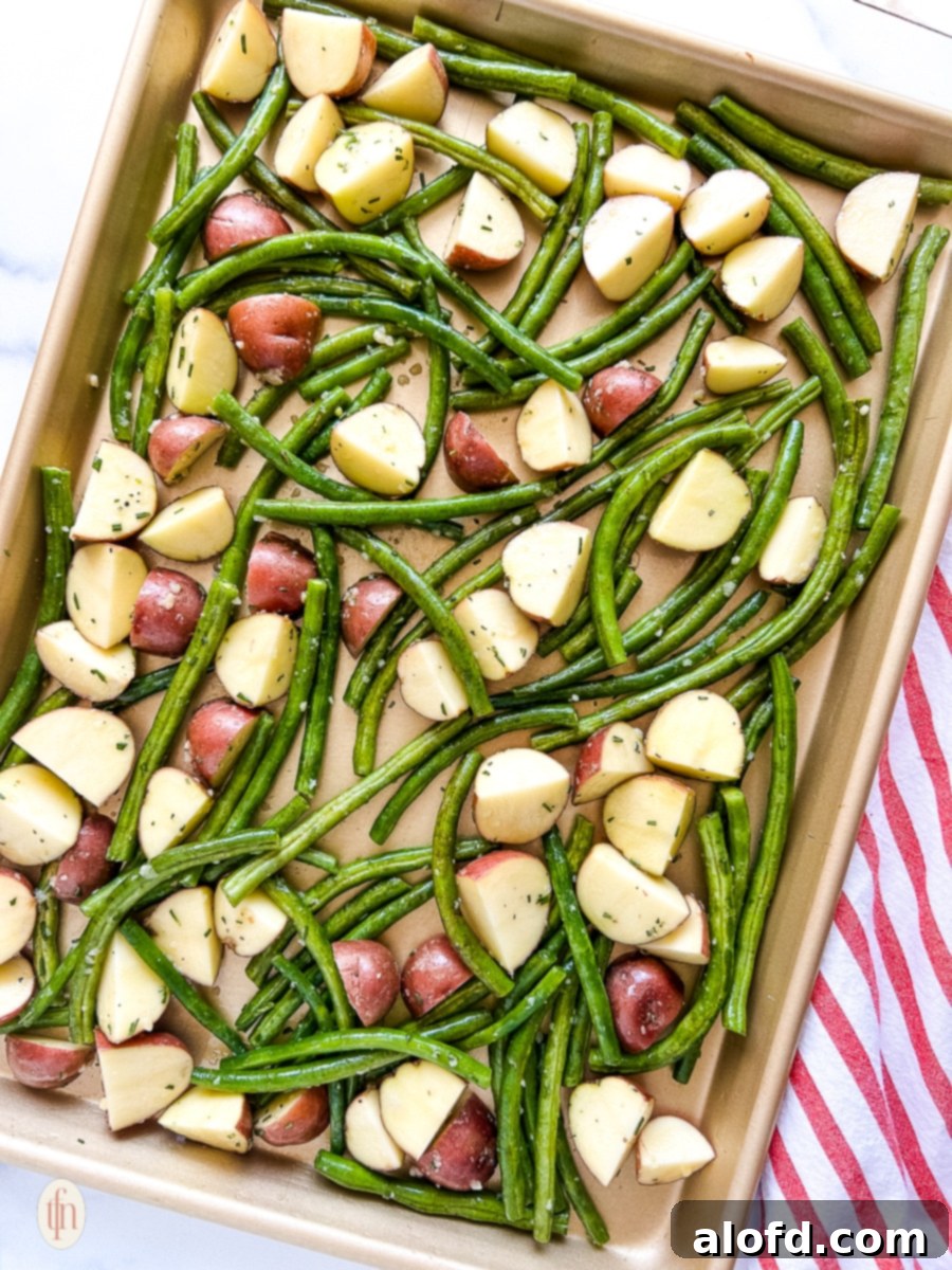 Garlic Herb Roasted Green Beans and Potatoes 6 A sheet pan filled with seasoned green beans and potatoes, spread in a single layer, ready for roasting.