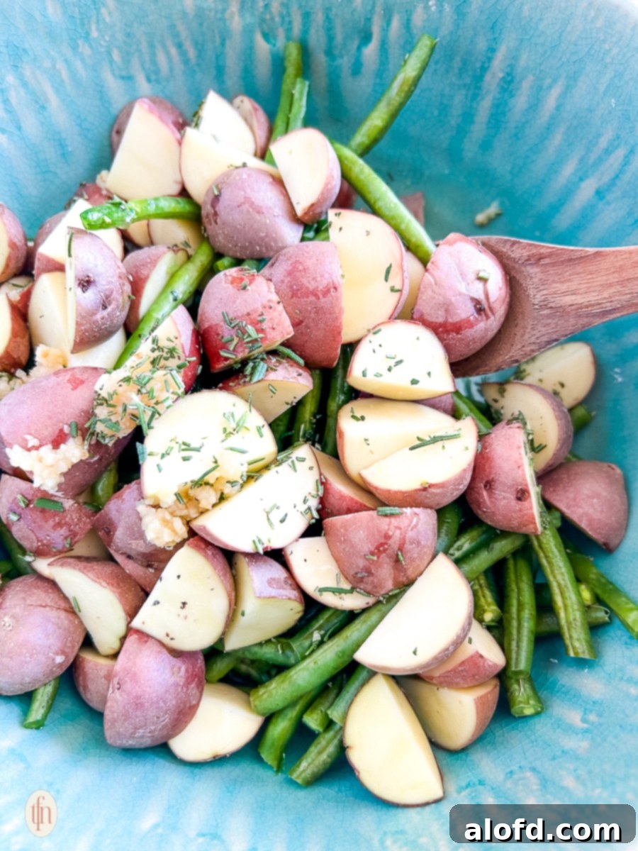 Garlic Herb Roasted Green Beans and Potatoes 7 A large mixing bowl containing roasted green beans and potatoes being gently tossed with a spoon.