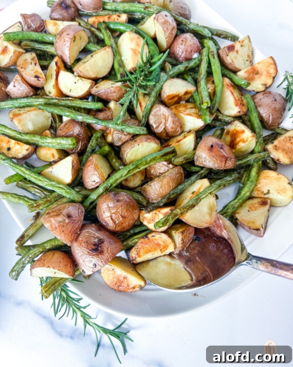 Garlic Herb Roasted Green Beans and Potatoes 8 A hand serving perfectly roasted green beans and potatoes from a baking sheet, ready for the table.