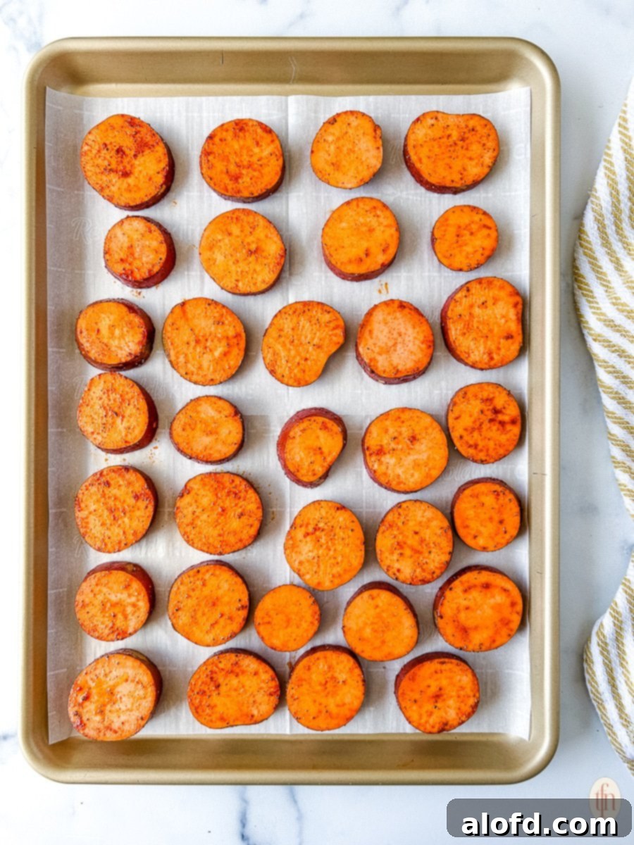 Sweet potato slices arranged in a single layer on a parchment-lined baking sheet, ready for roasting.