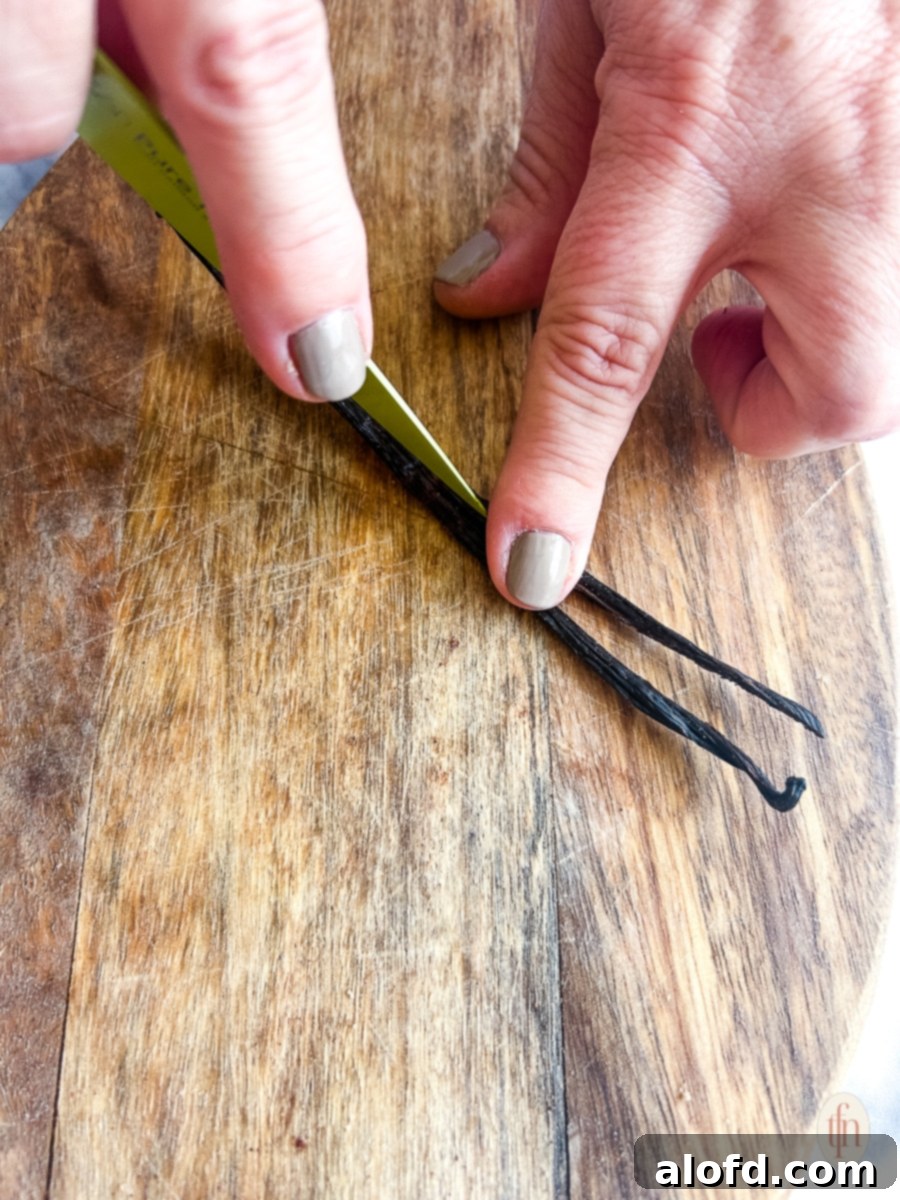 Velvety Vanilla Sauce for Bread Pudding 5 Fingers cutting a vanilla bean pod in half with a knife.