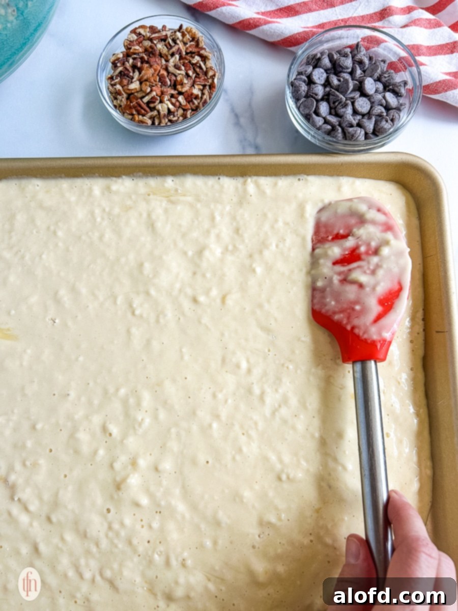 Effortless Sheet Pan Pancakes from Mix 6 Pancake batter being smoothed evenly across a sheet pan using a red silicone spatula, ready for toppings and baking.