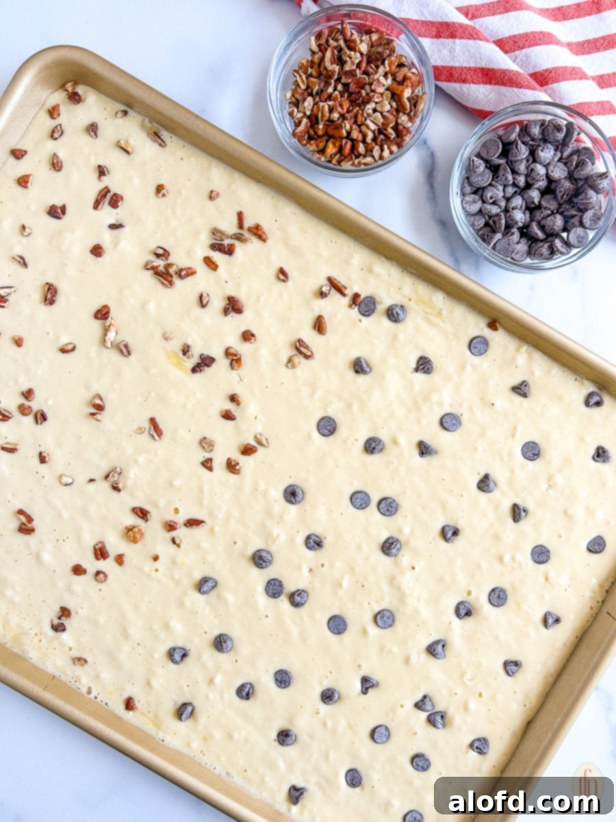 Effortless Sheet Pan Pancakes from Mix 7 A sheet pan filled with pancake batter, half topped with chocolate chips and the other half with blueberries, showcasing customizable topping options.