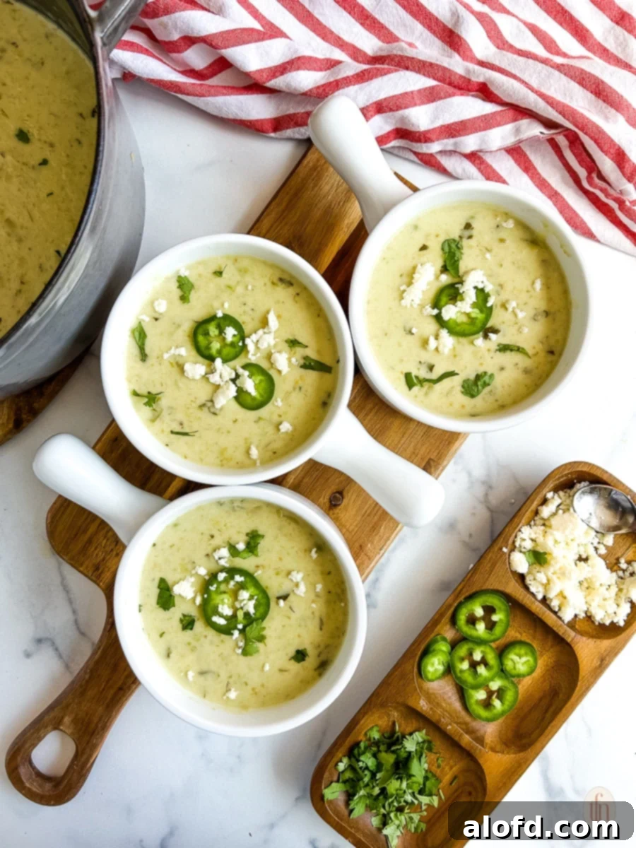 Three bowls of cream of jalapeno soup on a cutting board on a white background.