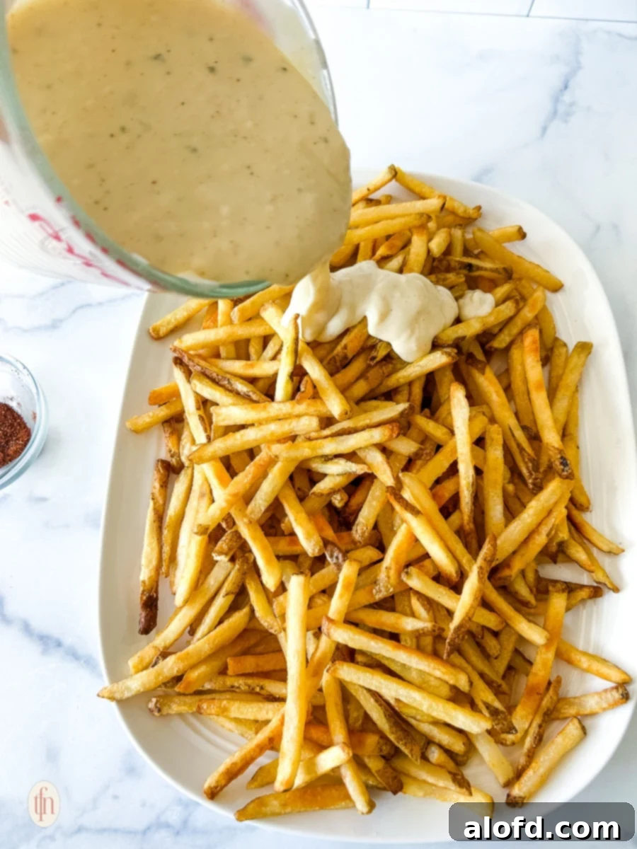 Voodoo Kitchen Fries 7 Pouring the rich, creamy Cajun ranch cheese sauce generously over a plate of freshly cooked, golden-brown French fries just before serving.