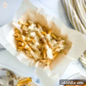 Voodoo Kitchen Fries 9 A basket filled with crispy French fries generously covered in a creamy, spicy Voodoo sauce, served on a white background.