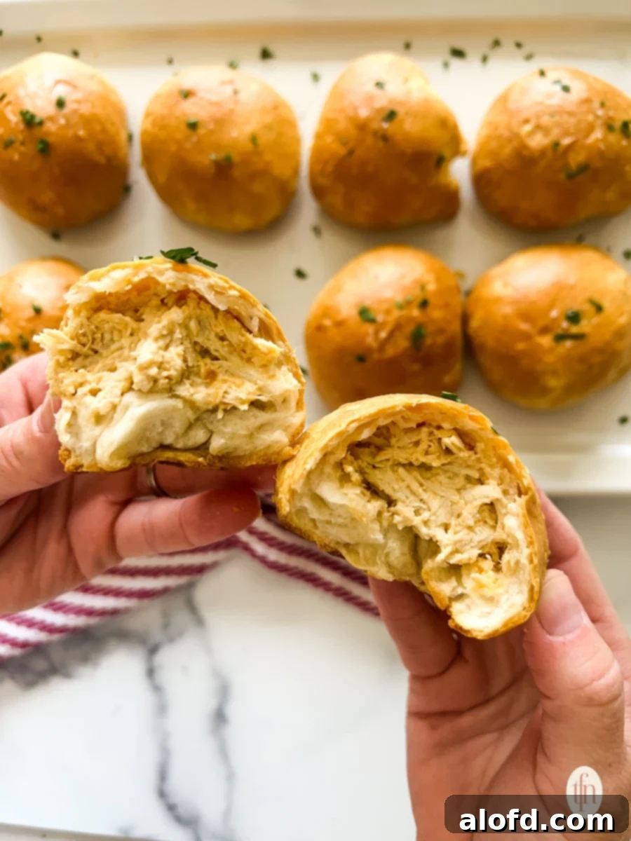 Fiery Buffalo Chicken Poppers 3 Hands holding a freshly baked buffalo chicken biscuit bomb, torn in two halves, revealing the melty, cheesy filling over a baking tray filled with more bombs.