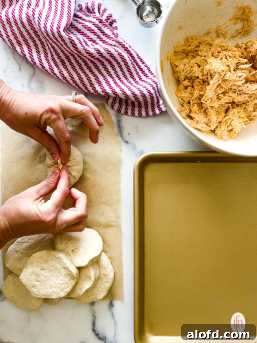Fiery Buffalo Chicken Poppers 8 Hands carefully pinching biscuit dough closed around a mound of buffalo chicken filling, ensuring a tight seal for the bomb.