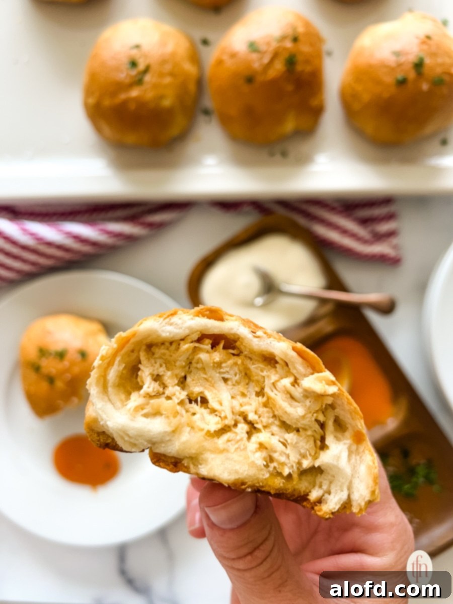 Fiery Buffalo Chicken Poppers 10 A hand holding one half of a buffalo chicken bomb, showcasing the gooey cheese and chicken filling, with a plate of other bombs and dipping sauces in the background.