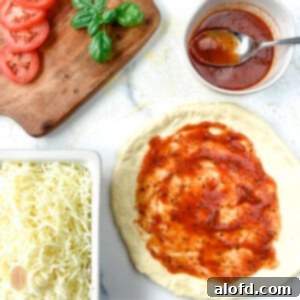 Sauce, cheese, fresh tomato slices and shredded mozzarella cheese surround a crust with red sauce on it.